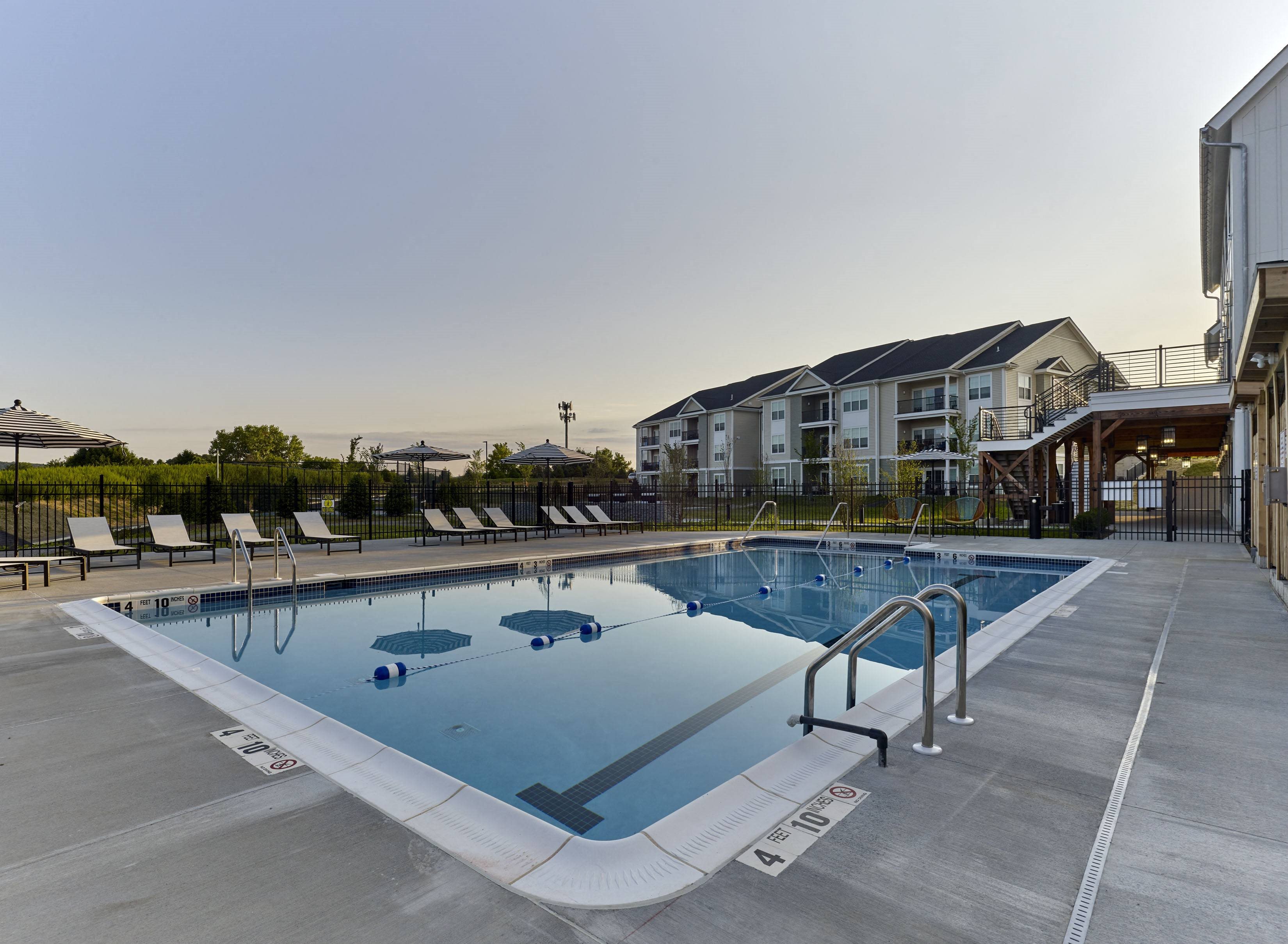 a swimming pool with chairs around it in front of an apartment building